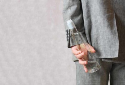 man hiding alcohol bottle behind back