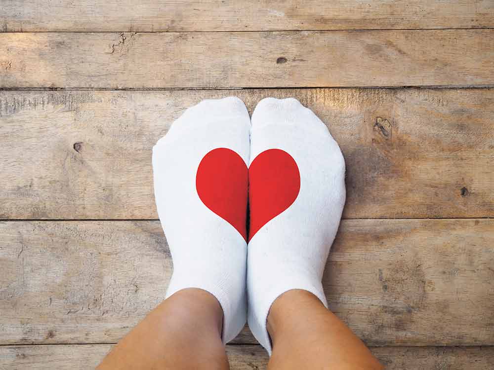 A close up of two feet with a pair of white socks and a red heart on them.