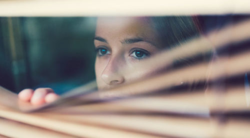 woman looking out a window through blinds