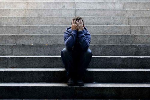 man sitting on steps holding face in his hands