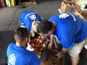 A screenshot from a video of three Beach House volunteers gathering produce in a warehouse.