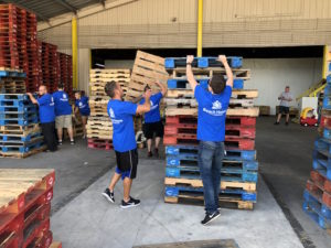 A group of young men with Beach House Recovery T shirts on, packing wood pallets.