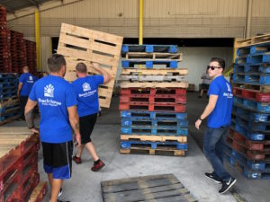 A group of young men with Beach House Recovery T shirts on, packing wood pallets.