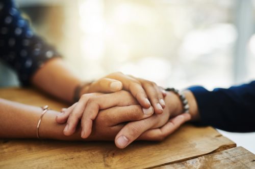 Two hands on a wooden table, symbolizing connection