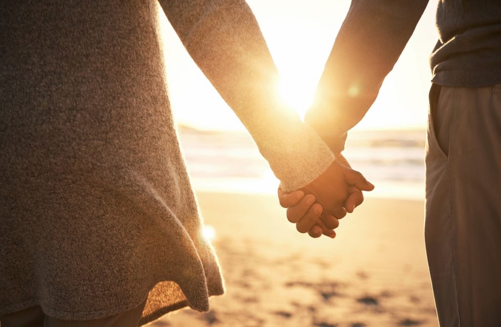 Two people watching the sunset while holding hands on the beach.