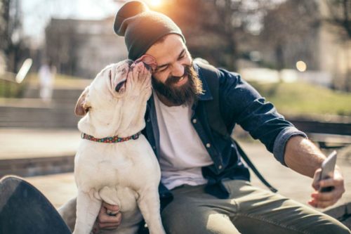 Man with beard and hat on skateboard with dog