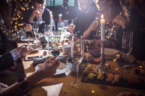 A group of friends sitting around a dinner table celebrating Christmas with glasses of champagne and food on the table.