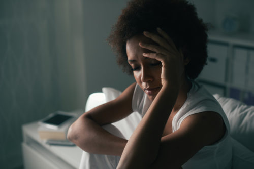A woman sitting up in bed with her head in her hands. She looks troubled.