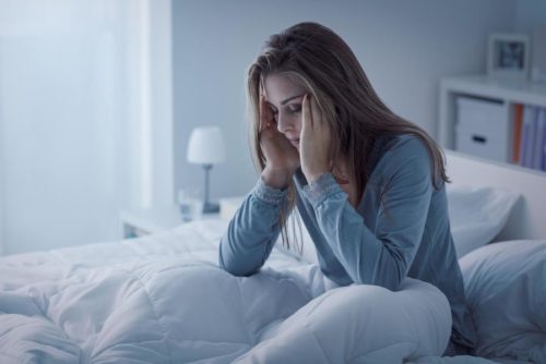 Distressed woman on bed, hands on head