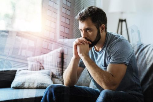 Man thoughtfully sitting on couch, hands on chin