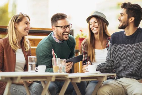 Four men and women sitting at a restaurant table sharing a joke. There are coffees and glasses of water on the table in front of them.