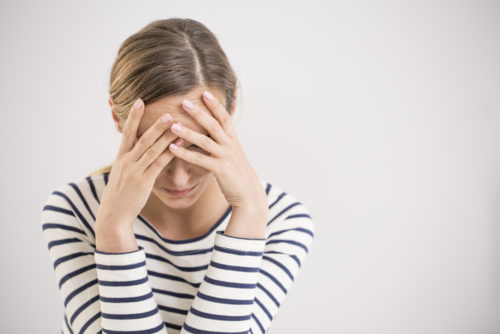 A portrait of a caucasian woman covering her face with her hands looking upset.