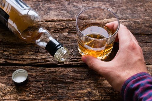 Man holding whiskey glass above bottle.