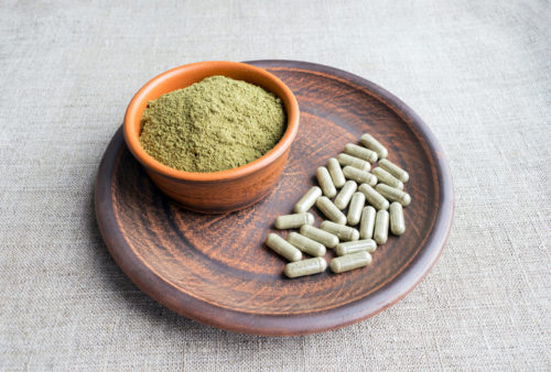 Green powder and capsules arranged on a wooden plate