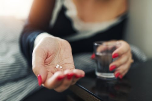 A woman holding a pill and glass of water