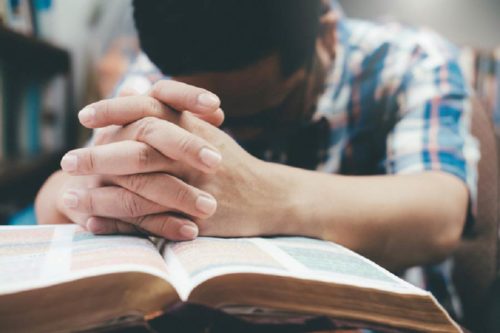 A young man praying over an open bible.