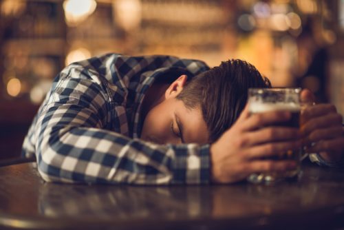 A young man passed out at a bar while holding a beer.
