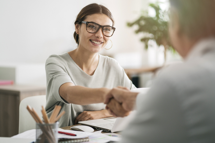 Woman in glasses shakes hands with a man at a desk.