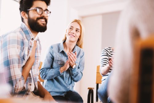 A group of men and women smiling and clapping while in a group therapy session.