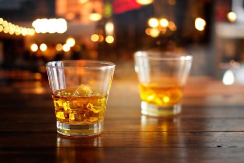 Two glasses of whiskey resting on a wooden surface