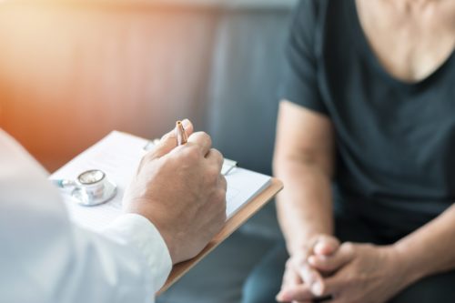 A male doctor filling out paperwork while talking to an older female patient.