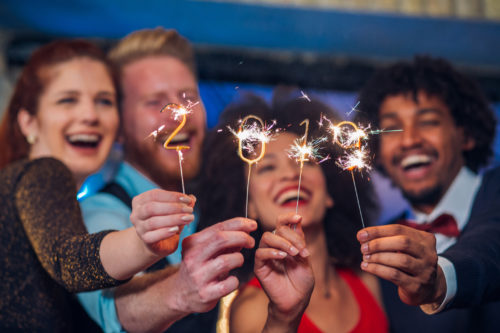 A group of smiling men and women holding up numbered sparklers. Together the sparklers show 2019.