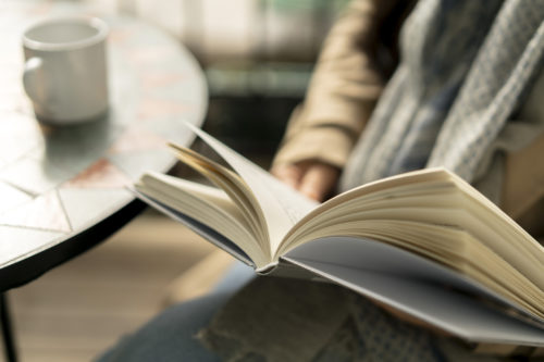 A close up of a woman sitting at a coffee table reading a book.