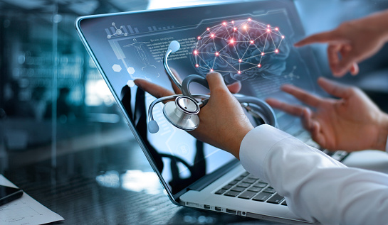 Medical doctors meeting and analysing brain scan results on a laptop with a stethoscope in hand.