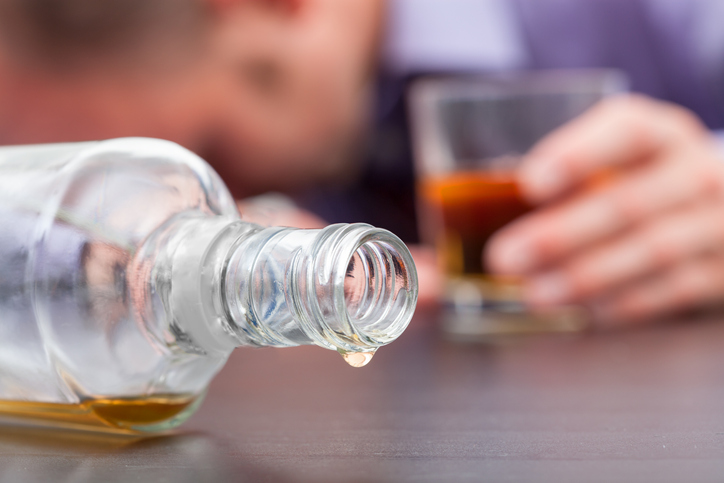 A liquor bottle toppled over with a hand holding a glass of liquor in the background.