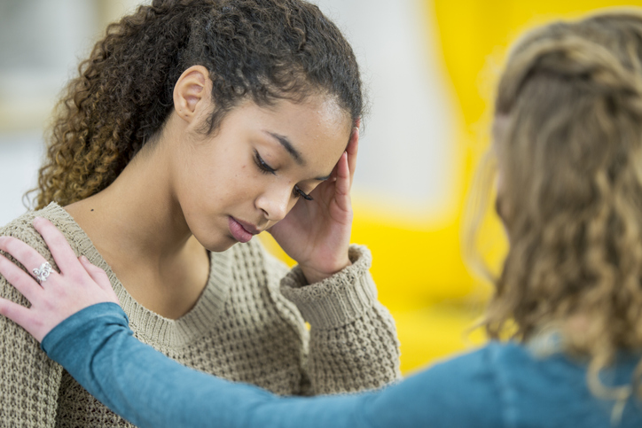 Two young women talking. One woman looks sad, and she is being comforted by her friend.