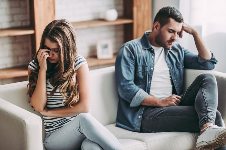 A male and female sitting on a couch during a therapy session. They are looking away from each other in frustration.