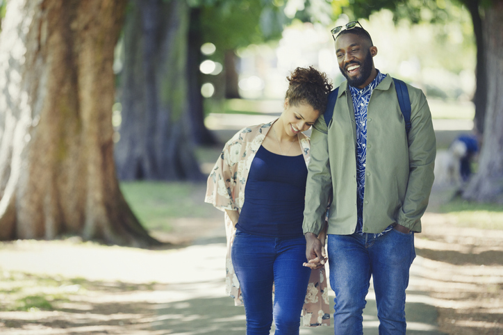 A smiling couple walking hand in hand through some trees.