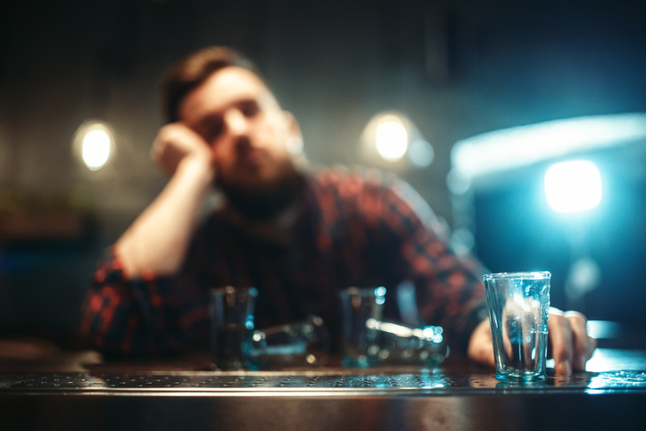 A drunk man sleeping at bar counter with empty shot glasses in the forefront of the photo.