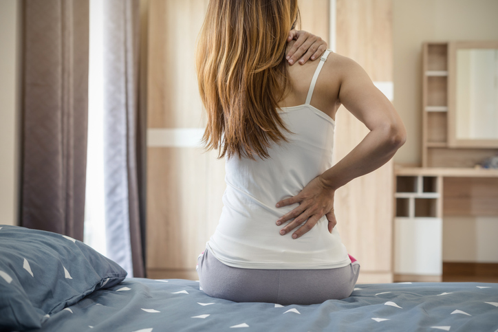 The back of a young woman suffering from backache while sitting on the bed