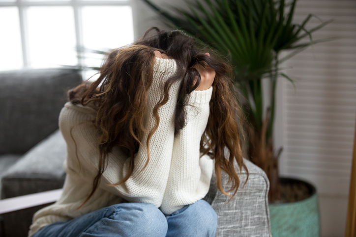 A women with brown hair holding her head in her hands in frustration, or sadness.