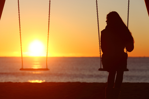the silhouette of a young women sitting on a sing at the beach while the sun sets.