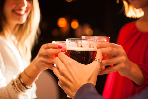 Friends smiling and sharing a drink. The glasses of alcohol are the focus of the image.