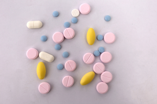 A variety of pink, white, blue and yellow prescription drugs laid out on a table.