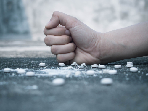A fist crushing white tablets on a table top.