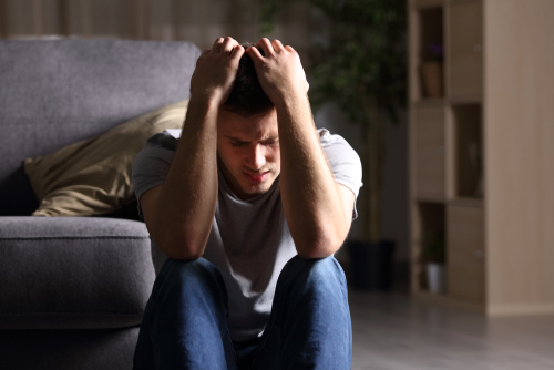 A young man sitting on the floor with is head in his hands in frustration or sadness.