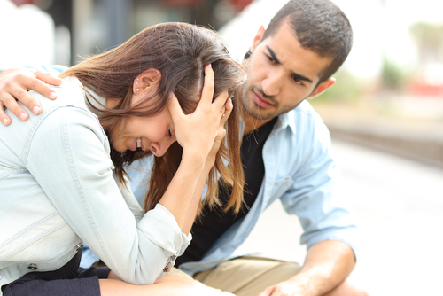 A young man comforting a young women who has her head in her hands crying.