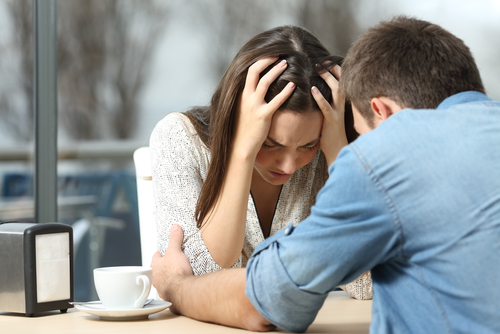 A young man comforting a young woman who has her head in her hands crying.