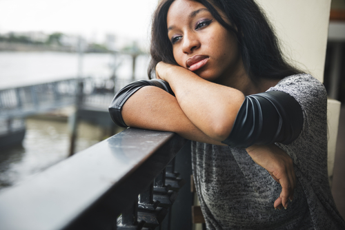 A young women sitting on a balcony looking sad.