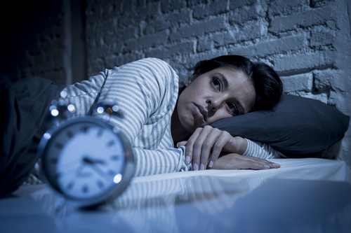 A young women lying in bed looking away sadly with a clock in the forefront.