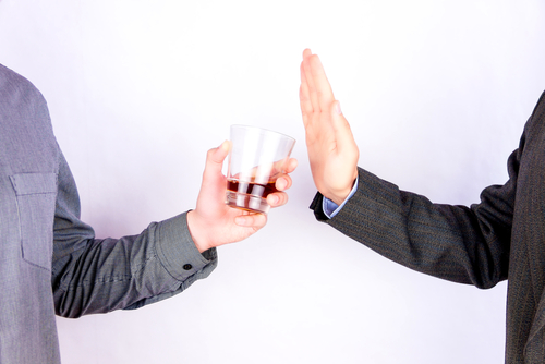 A man being offered a glass of alcohol by another, and refusing it.