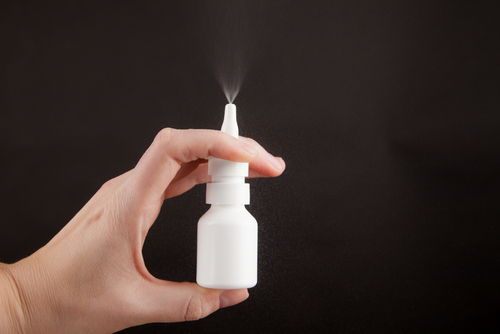 A hand spraying a bottle of nasal spray into the air.