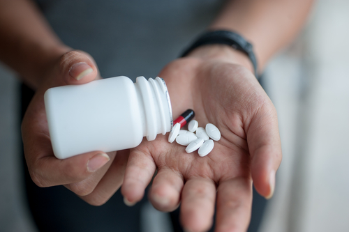 The hands of a young man shaking prescription pills into his hand.