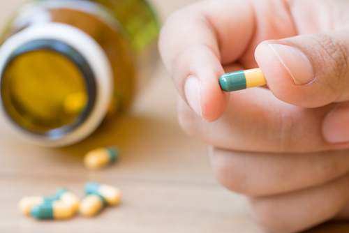 A hand holding a Tramadol medicine capsule with other capsules scattered on the table.