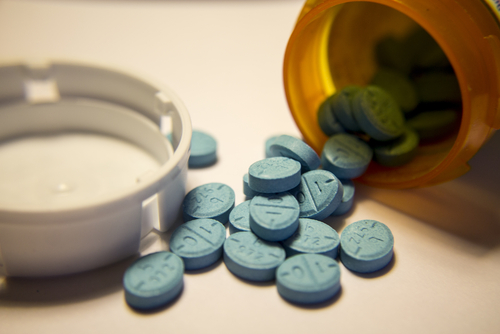 A bottle of blue Adderall pills spilling out on a white counter top