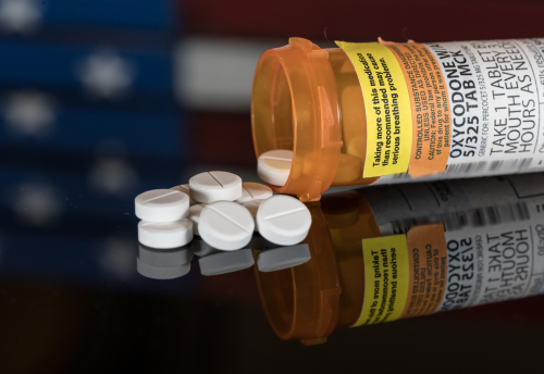 A bottle of Oxycodone toppled over and spilling out on a black counter.